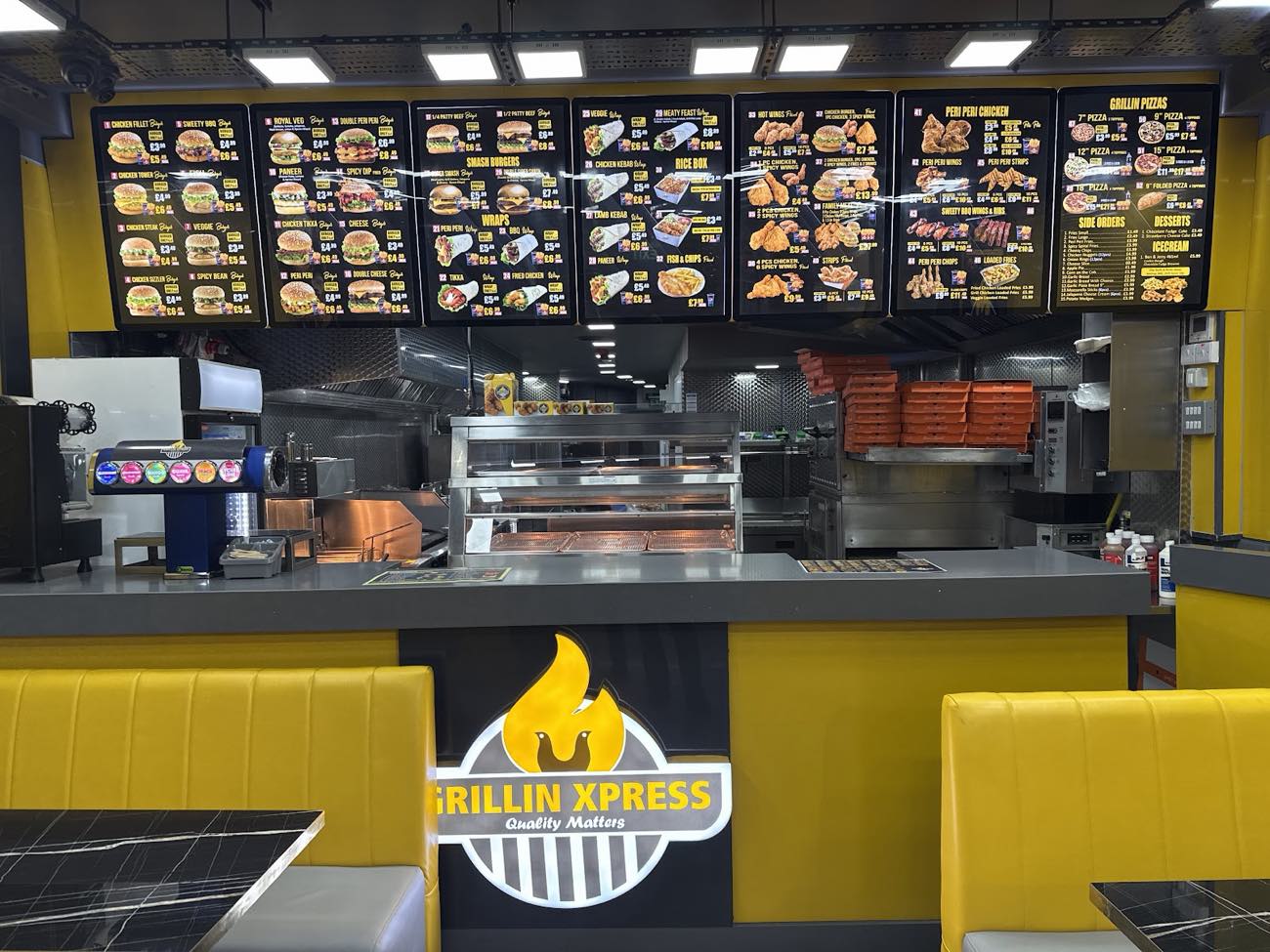 The counter and lit menu boards inside Grillin Xpress, with the flame logo on the front